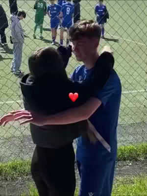 The cover image shows two people embracing each other. A red heart is superimposed between then. In the background a blurry scene with people wearing sports uniforms, likely soccer jerseys, can be distinguished, close to a wire fence.