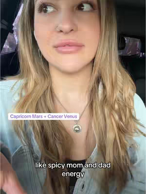 A selfie-style video cover image featuring a woman with long blonde hair. The woman is looking slightly off-camera. Overlay text reads 'Capricorn Mars + Cancer Venus' in a white rectangle, and below it, the text reads 'like spicy mom and dad energy'.