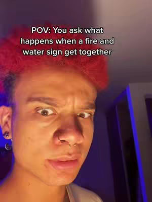 The cover image is a close-up shot of a person's face with bright red hair. The person is looking directly at the viewer with a slightly squinting expression. Text overlayed on the image reads, \"POV: You ask what happens when a fire and water sign get together\". The overall color palette is warm, with orange and red tones dominating.