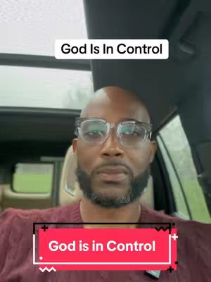 The cover image features a bald Black man wearing glasses and a maroon shirt. Above his head is a white rectangle with the text "God Is In Control." Below him, a red rectangle with the same text is overlaid, with curved edges. The background appears to be interior of a car.