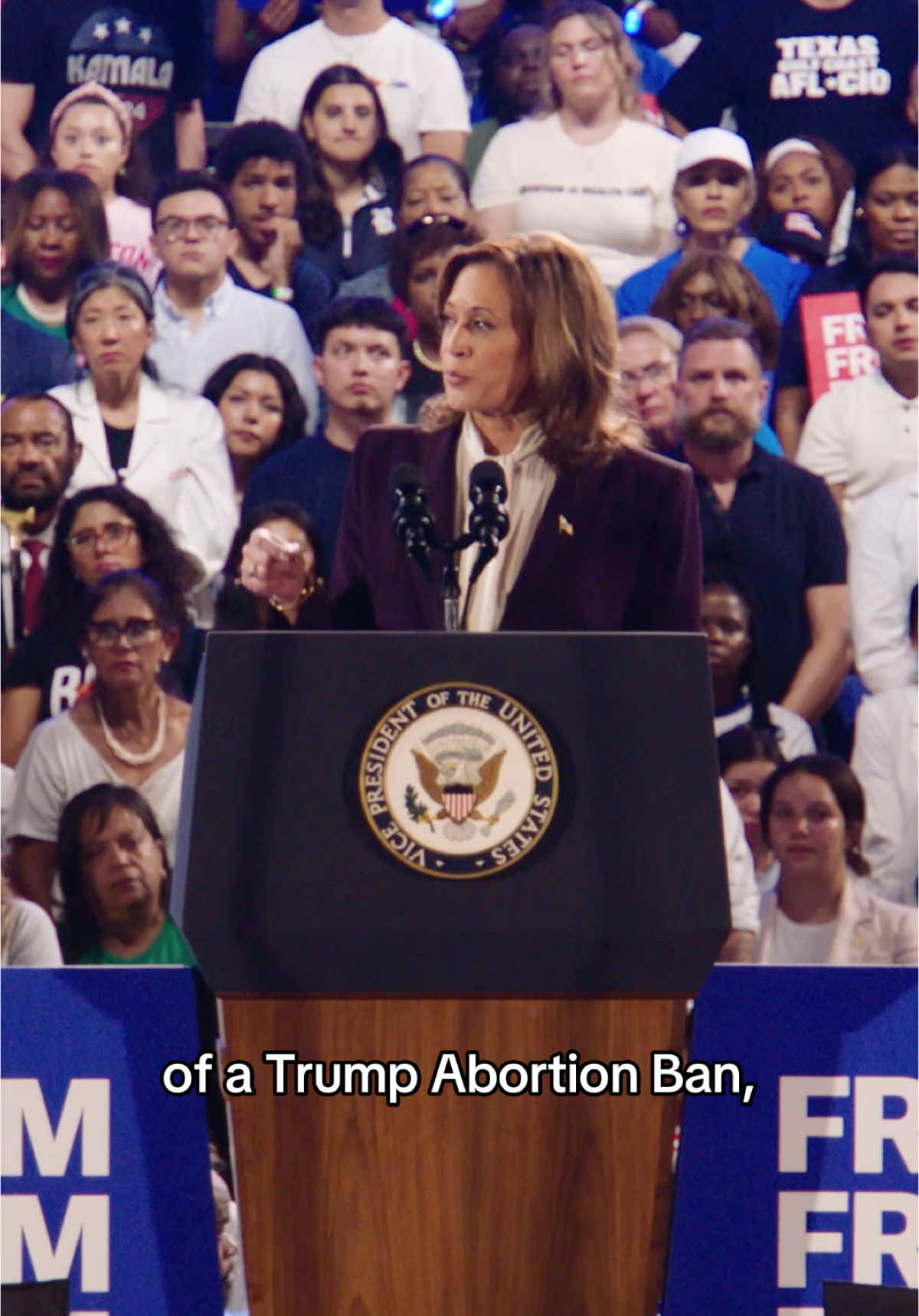 The cover image shows a politician, potentially Kamala Harris, addressing a crowd. She stands behind a podium bearing the presidential seal, with a diverse audience visible in the background. The image is well-lit, with a focus on the speaker. A text overlay at the bottom reads "of a Trump Abortion Ban."