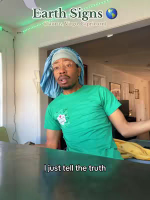 A man in a teal cap and green t-shirt is in a well-lit space. The overhead text indicates a focus on Earth signs. The man seems to be addressing the camera from a table setting, expressing a message with a slight tilt of his head and a confident expression.