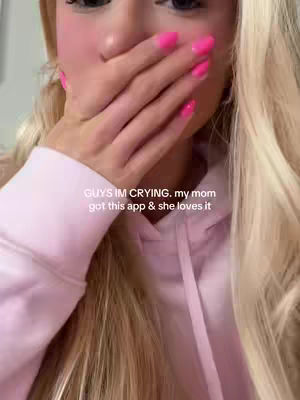 A selfie-style shot with the creator covering their mouth with a hand, displaying bright pink nail polish. The background is blurred, focusing on the upper body and face. Text overlay with the sentence: “GUYS IM CRYING. my mom got this app & she loves it.”