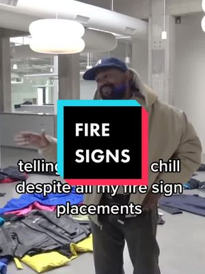 A man in a grey outfit and a blue cap stands in a room with folded clothes. A rectangular graphic saying FIRE SIGNS is placed on him.
