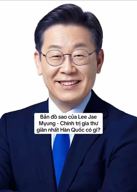 The image features a mature Asian man with short, dark hair, wearing round glasses and a dark suit with a blue tie. He is smiling at the camera. A white box with text overlayed on the bottom half reads, 'Bản đồ sao của Lee Jae Myung- Chính trị gia thư giãn nhất Hàn Quốc có gì?'
