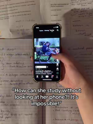 An eye-level shot shows a hand holding a phone displaying a video of a woman sitting on a bench, appearing to study. The phone is positioned in the center, with the background showing handwritten notes. The overlay text reads, How can she study without looking at her phone?! It's impossible!