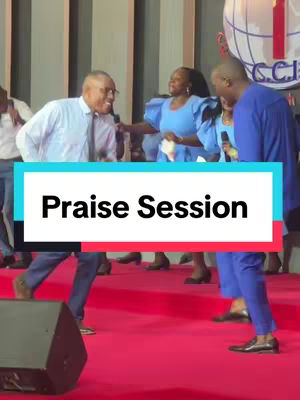 The image shows a stage during a church event, the stage is covered in a vivid red carpet, and a group of people are singing and worshipping. The central figure is a man in a suit jacket holding a microphone, with others visible at the background.