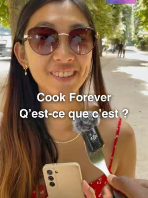 A woman with sunglasses is holding a phone and a microphone clipped to a fork. The background is a blurred outdoor scene.