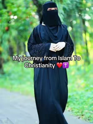 A woman in a black abaya, head covering, and face veil is standing outdoors on a pathway. The background is blurred green foliage.