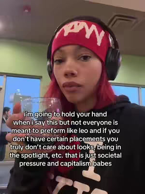 A person with red hair is holding a glass, wearing a red beanie with white text and headphones. Text overlayed on the image.