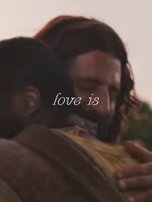 The cover image shows a close-up of two people embracing. The person on the right, likely Jesus, has long hair and a beard, his head gently resting on the shoulder of the person on the left. The image is softly lit. The text 'love is' is overlayed.