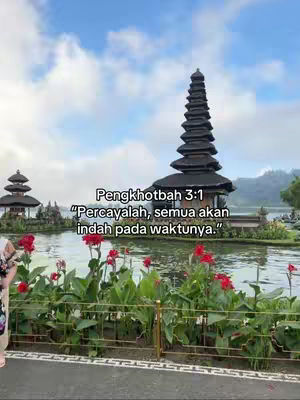 The image captures a serene landscape with a body of water in the foreground, featuring vibrant red flowers and lush greenery. Two traditional structures are visible, with a multi-tiered pagoda as the central focus. The background features a light blue sky and white clouds, enhancing the overall peaceful atmosphere. Text overlays on the image convey a religious message.