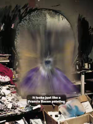 The image shows a blurred interior of an old studio, filled with cluttered objects. A central circular, bright shape dominates the view, possibly a large mirror or light source that the focus falls upon. The foreground is filled with various items, boxes, and materials suggesting a messy workspace, with a text overlay at the bottom.