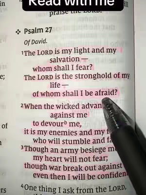 The image shows an open book with a page of the Bible. The text is highlighted with pink marker. A black pen is pointing to the highlighted text.