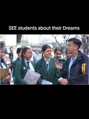 A group of students in school uniforms are gathered outdoors, with a young man speaking to them while holding a microphone. The scene suggests an interview or discussion, and the backdrop is a blurry street scene.