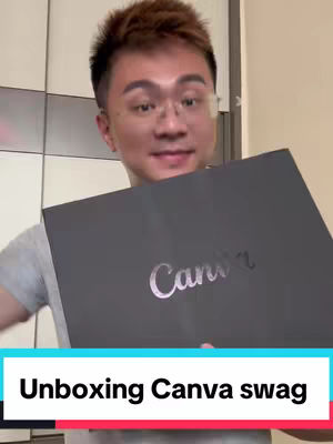 A man in a gray t-shirt holds a large black box with the 'Canva' logo in silver. The background is a room with a white door and light-colored wall. The image is well-lit. Below, there's a colorful bar with the video title.