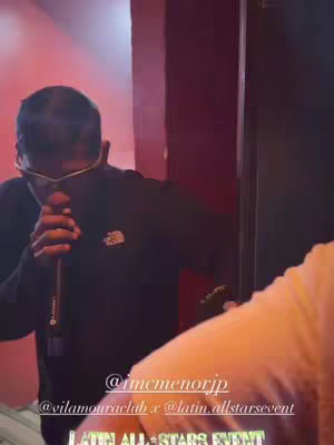 The cover image is a medium shot taken in what appears to be a club or performance venue with reddish lighting.  A man is holding a microphone close to his face. He is wearing sunglasses, a black jacket. His pose and equipment suggest he is performing or about to perform, possibly singing.