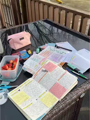 An open Bible highlighted with pinks and yellows sits on a glass table surrounded by stationary supplies, fresh fruit, and a pink cosmetic bag. The outdoor setting suggests a casual study session. The text overlay reads "I win."