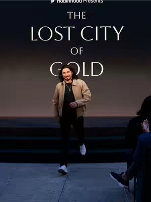 The cover image features a man standing on a stage with a dark background and text overlay. The man is wearing a jacket and black pants and has long hair. Text overlay: 'The Lost City of Gold'.