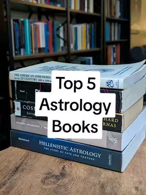 A stack of books on a wooden surface, with a blurred background of bookshelves. The cover image features a white, square graphic in the center with the text "Top 5 Astrology Books" in a bold, sans-serif font. The books have titles and author names, some with visible colored spines of different thicknesses. The layout is simple, with the focus on the book stack. The color palette includes shades of blue, brown, white, and grey.