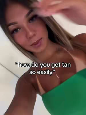 A young woman with long hair is the focus of the image, captured from the chest up. She has fair skin, dark eyebrows, and full lips. She's wearing a green top that contrasts with her skin tone. The lighting appears natural, and the background is a blurred or out-of-focus interior or outdoor setting. Text overlayed has a simple font and white color.