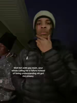 A young Black man in a beanie and puffer jacket looks directly at the camera in a dimly lit outdoor setting. Text overlays the video.