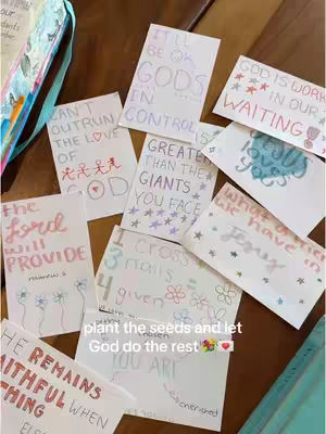 The image showcases a collection of handwritten Bible verses on small, rectangular cards. They are scattered across a wooden surface, creating a visually engaging arrangement. Each card features colorful handwriting and simple illustrations, emphasizing key biblical messages. The layout is casual and inviting, with a focus on the uplifting and inspirational content.