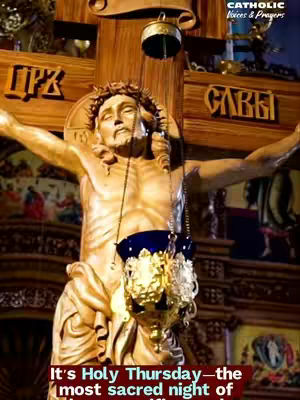 The image shows a golden statue of Jesus on the cross. The statue is centrally positioned, with arms outstretched. Above, a wooden cross structure supports the sculpture. Hanging in front of Jesus is a decorative censer with a golden exterior and a colored interior. The background consists of a mix of dimly lit architectural details and decorative elements.