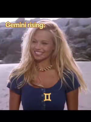 A woman with long blonde hair smiles on a beach, wearing a blue top. The text overlay 'Gemini rising:' is at the top. A golden Gemini symbol is on the top of the top.