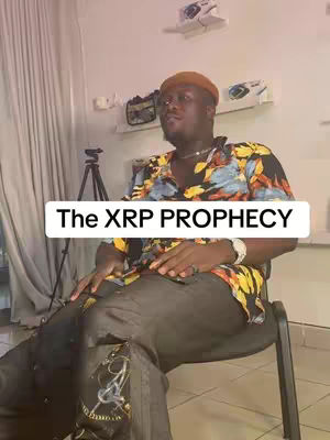 A man in a colorful shirt sits on a chair, looking slightly upward. A text overlay reads "The XRP PROPHECY."
