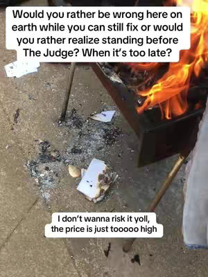 A close-up shot of a fire pit with flames, ashes, and partially burned paper, framed from a high angle.