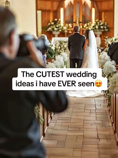 A wedding ceremony is taking place inside a church. The focus is on the bride and groom standing at the altar, with a photographer taking a photo in the foreground. The church features a high ceiling, stained-glass windows, and floral decorations.