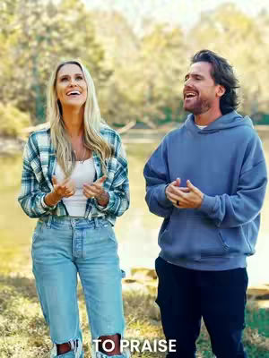 The cover image shows a woman on the left and a man on the right, both standing outdoors in front of a blurred background of trees and a body of water. They are both looking up. The woman is wearing a light colored top, blue jeans, and a plaid shirt. The man is wearing a blue hoodie and black pants. Text in white at the bottom of the image says "TO PRAISE".