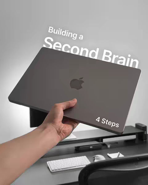 A person holding a MacBook laptop with overlaid text: 'Building a Second Brain' and '4 Steps.' The hand is holding the laptop against a blurred gradient background, suggesting a workspace setting.