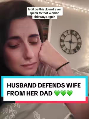 The cover image shows a close-up of a woman's face, with her head resting on her hand and eyes closed. In the lower part of the image, there is a vibrant teal rectangular bar with white text that reads: 'HUSBAND DEFENDS WIFE FROM HER DAD' with three green heart emojis.  Above her head is a small white rectangular text bubble with the text: 'let it be this do not ever speak to that woman sideways again'. Behind the woman, a wall with a round clock. The overall color scheme is warm, from the woman's skin tones to the soft backdrop, contrasted by the bright text overlay.
