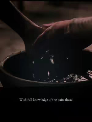 The image displays a close-up of hands interacting with water in a dark, possibly religious setting. One hand is holding and pouring water into a dark basin. The overall lighting is dim, creating a sense of solemnity or intimacy.
