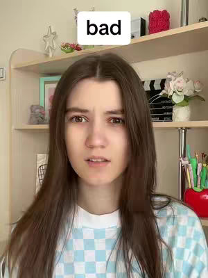A young woman with long brown hair stands in front of a shelf filled with decorative items. She is wearing a light blue and white checkered top. A text overlay reading 'bad' is positioned above her head. She has a slight grimace on her face, as if she is uncertain or disapproving. The background includes a wooden shelf with various items on display, creating a homey and casual environment.