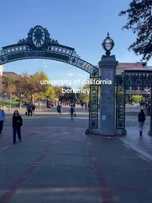 The image shows a large ornate archway with the text "university of california berkeley" in front of a blue sky. People are walking through the archway. The ground is made of large square tiles and in the distance buildings and trees can be seen.