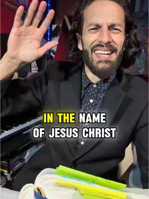 A man in a blazer is waving his left hand, there is a piano on the bottom left, with text overlayed near the bottom center.