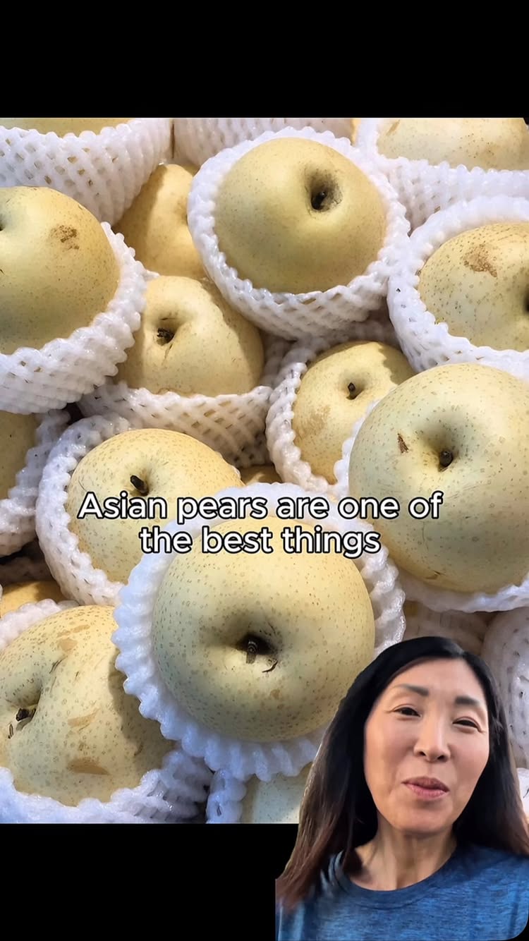 The image shows a close-up view with many Asian pears. The pears are round, pale yellow, and each is protected by a white foam net. The foreground also includes a woman with black hair, smiling at the camera, who is likely the creator.