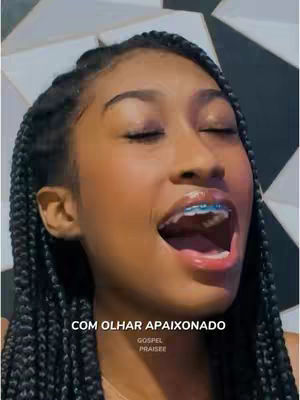 A close-up shot of a young woman with long, braided hair and braces smiling with her eyes closed. The background is out of focus, with a black and white geometric design. Text overlays on the bottom of the image.