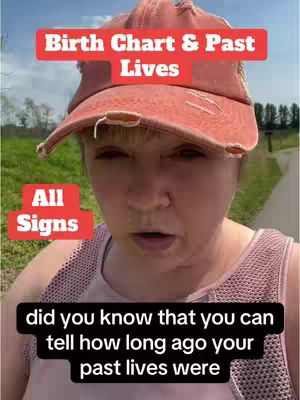 A woman in a pink baseball cap and tank top walks on a path in a park, looking toward the camera. Text overlays read "Birth Chart & Past Lives", "All Signs", and a lower text overlay states, "did you know that you can tell how long ago your past lives were".