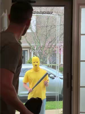 A person stands in a doorway looking at someone in a yellow hat with a bat. The person in the doorway's back is to the camera. The person in the hat is in front of a house and car.
