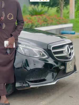 A man in a brown outfit is partially visible on the left, with a black Mercedes-Benz car parked in front. The setting appears to be outdoors, possibly a garage.