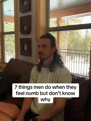 A man with dark hair and a mustache is sitting on a brown couch, looking off to the side with his eyes closed. Overlay text in a white rectangular box reads: '7 things men do when they feel numb but don't know why.' The background includes windows and wooden paneling.