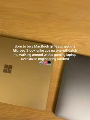 The cover image shows two laptops resting on a wooden surface. The laptop on the left is gold-colored, slightly angled toward the viewer, with the Microsoft logo visible. The other laptop, on the right, is silver or gray and is partially visible, with a blurred background. Text overlay is on the left part of the screen.