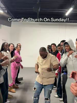 A group of diverse people stand in a large, well-lit room. The main subject, a man in a tan shirt and ripped jeans, is dancing in the center, with others on either side. A text overlay states, 'Come To Church On Sunday!!' above the group.
