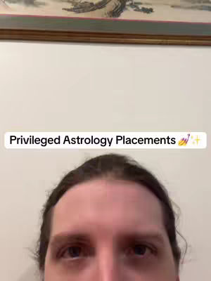 The cover image is a selfie from the chest up, featuring a person against a plain white wall with the top half of the image showing a portion of a framed picture. The person has light skin, dark hair, and is looking at the camera. Overlaying the image is a text bar that reads, “Privileged Astrology Placements” in a white font with a few emojis.
