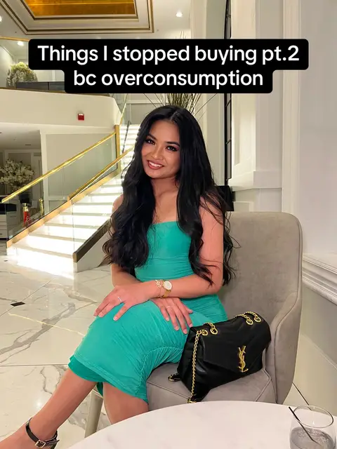 A woman in a green dress sits in a well-lit, upscale room with a black purse and a watch. Text at the top says, "Things I stopped buying pt.2 bc overconsumption".