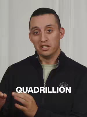 A man with short dark hair, wearing a black zip-up jacket, stands against a white background. Bold white text reading 'QUADRILLION' is overlaid on the lower portion of the image.